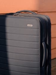 Partial view of an Away grey soft-side carry-on suitcase against a pink background.