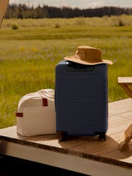 A navy suitcase on a deck next to a sand duffle bag.