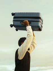 A man holding a Coast PC Flex suitcase over his head.