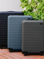 An assorted suitcase set of Away luggage. A Bigger Carry-On in asphalt, The Medium in coast blue, and a large checked size in navy blue.
