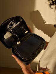 A person holding an Away Large Tech Case in black in front of them filled with tech accessories.
