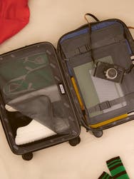 An open view of an Away carry-on suitcase filled with various personal items such as a camera and shoes.