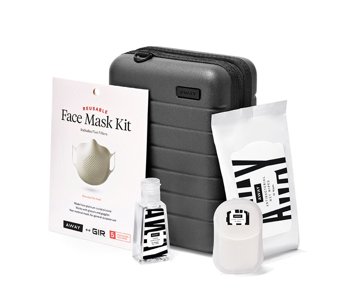 Mini suitcase in asphalt shown behind a bottle of hand sanitizer, wipes, soap sheets and mask.