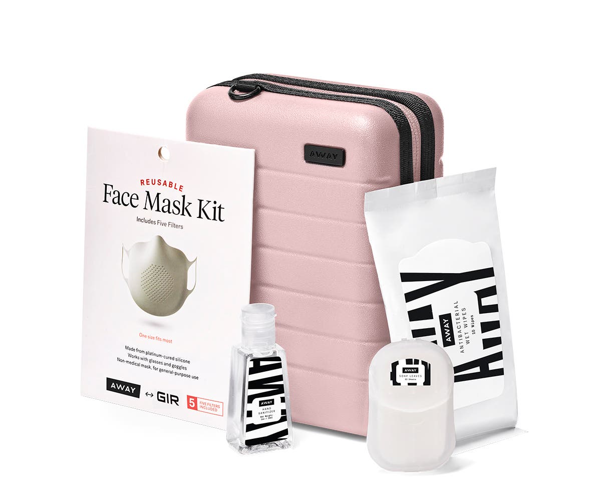 Mini suitcase in blush shown behind a bottle of hand sanitizer, wipes, soap sheets and mask.