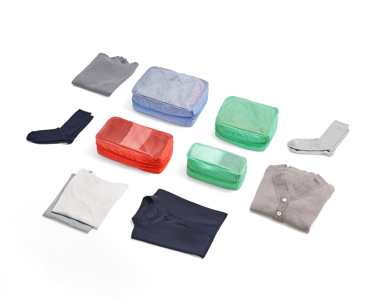 Large and small size packing cubes in red, green and light blue organized with clothing items with carefully folded socks and shirts around them.