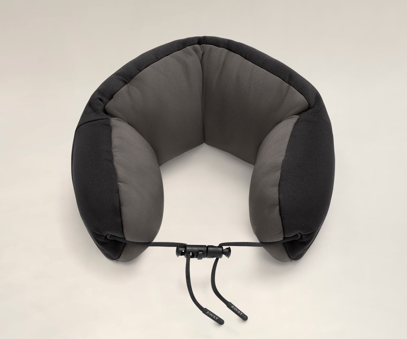 Aerial angled view of a black and grey travel neck pillow with a string loop on one side.