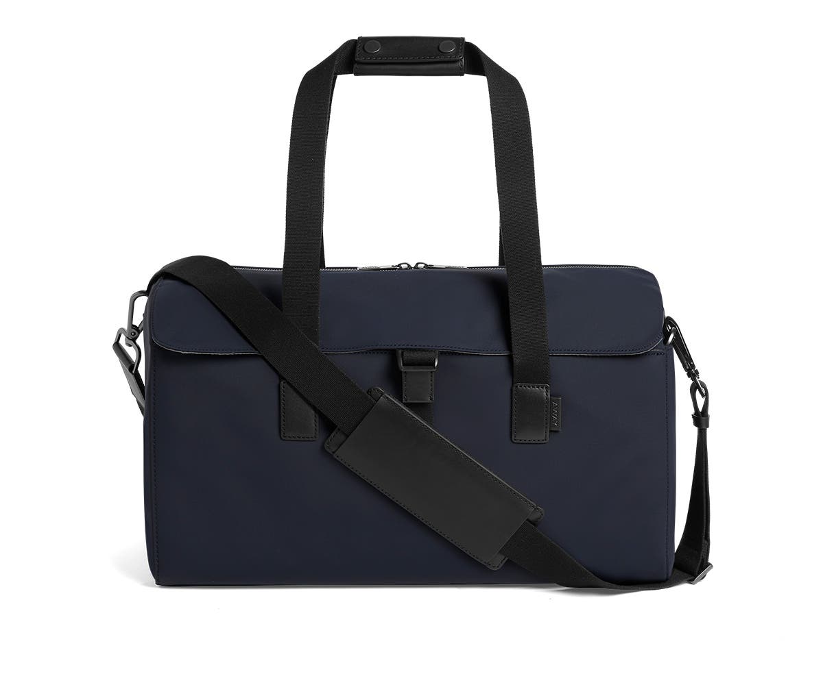 Flap black duffle bag in navy with raised handles and shoulder strap across the bag.
