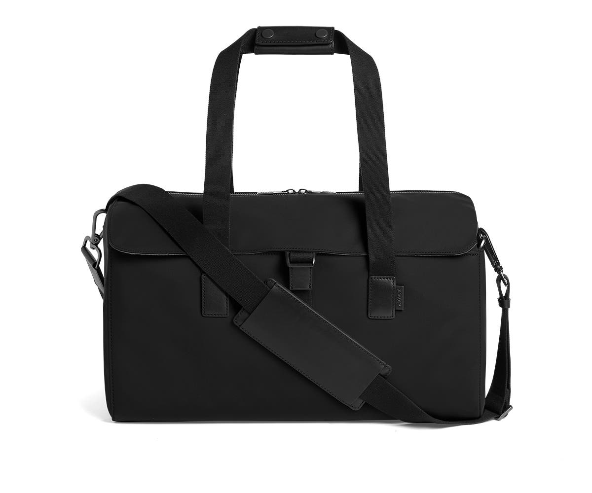 Flap black duffle bag in black with raised handles and shoulder strap across the bag.
