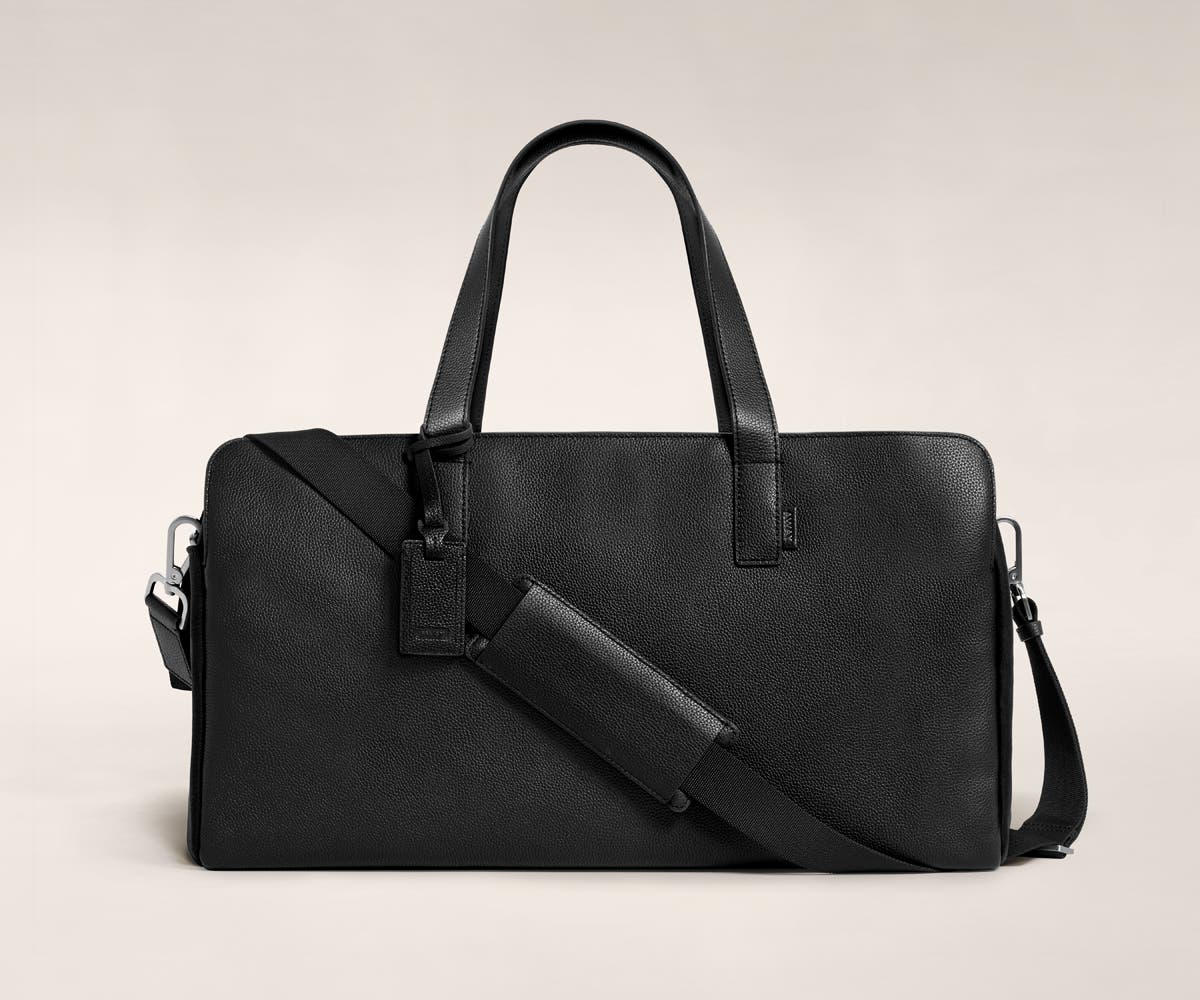 Three pocket duffle in black leather with raised handles and shoulder strap across the bag.