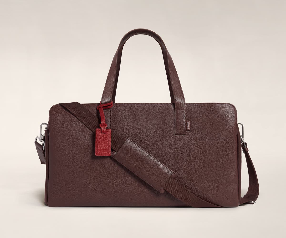 Three pocket duffle in Clove leather with raised handles and shoulder strap across the bag.